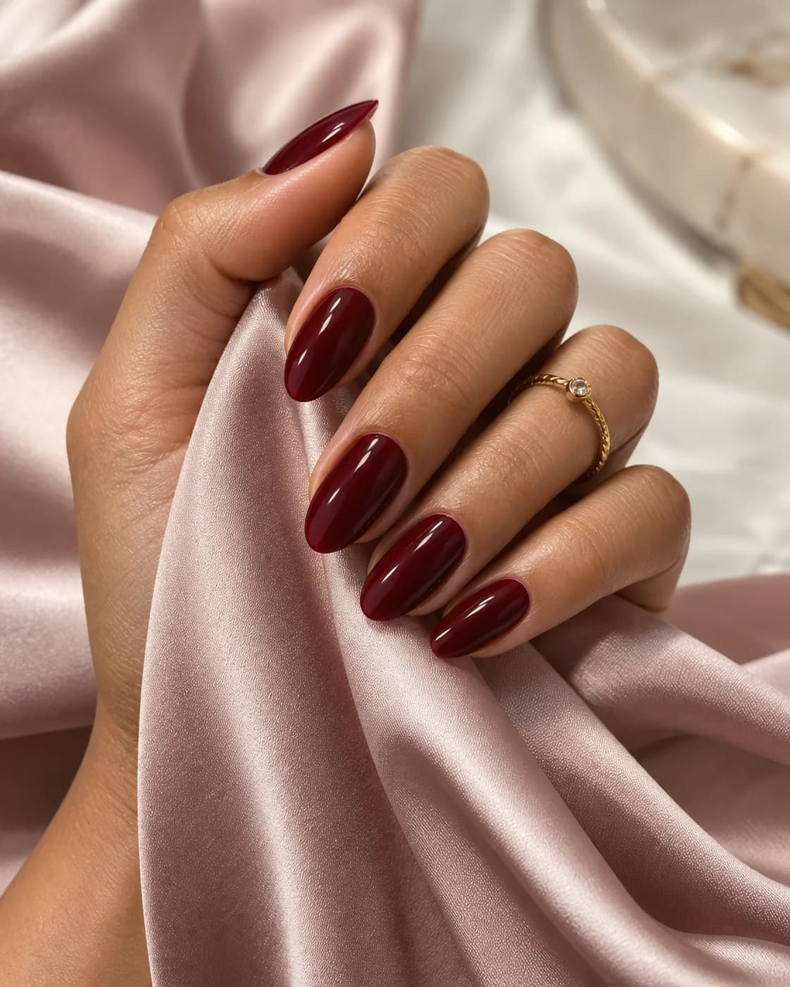Glossy burgundy almond nail inspiration against soft blush satin